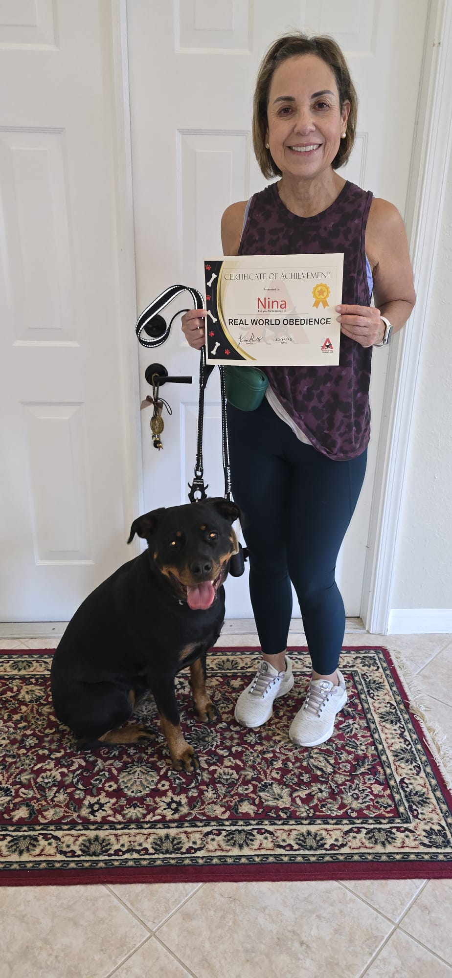 A client holding Nina's training certificate with her Rottweiler sitting calmly on leash.